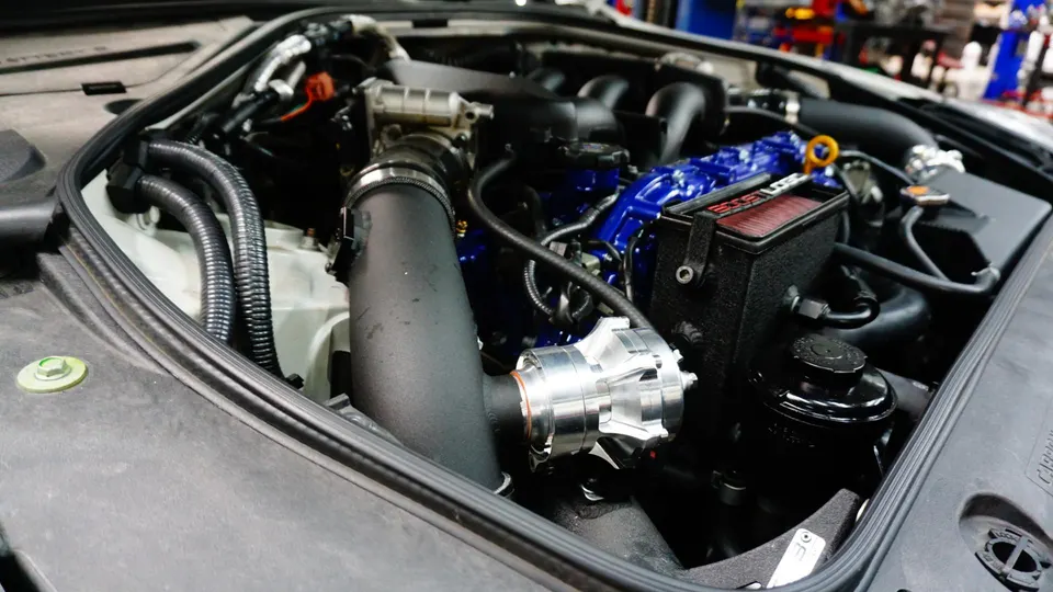 Close-up of a high-performance engine bay featuring an aftermarket intake, blow-off valve, and blue engine components.