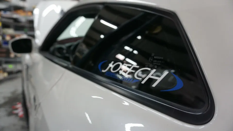 A close-up of a white car's rear quarter window featuring a Jotech Motorsports sticker.