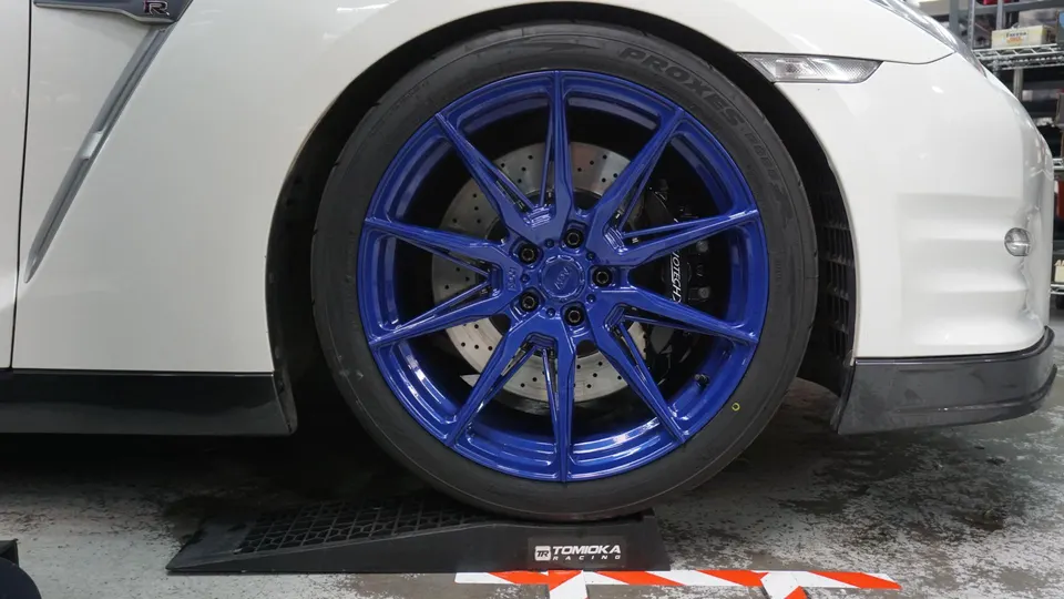 White Nissan GT-R with blue aftermarket wheels, Toyo Proxes tires, and Jotech brakes on a car ramp in a shop.