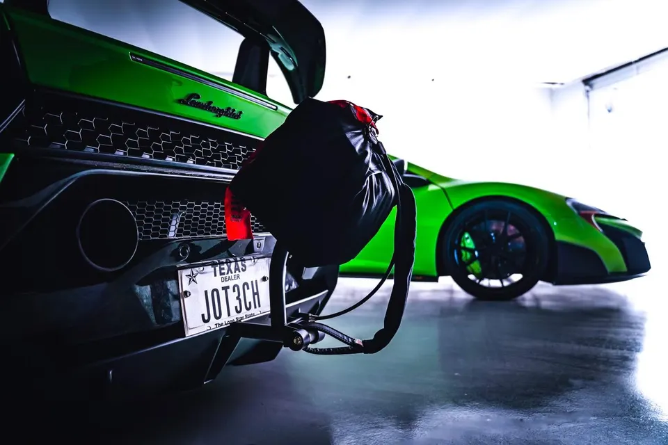 Rear view of a green Lamborghini with a black bag hanging, parked next to a green McLaren in a clean garage.