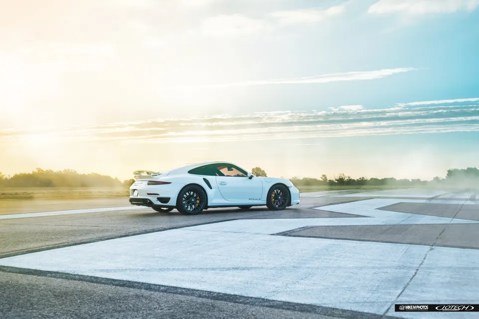White Porsche 911 Turbo S on an airfield at sunset, showcasing its sleek design and performance stance.