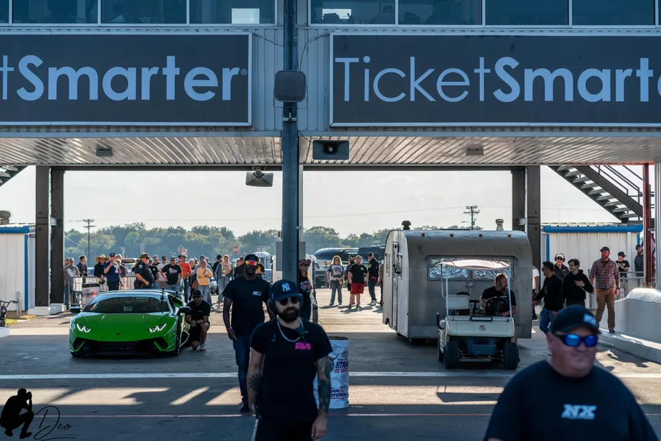 Green Lamborghini Huracan at a drag strip entrance with a crowd of people and TicketSmarter signs overhead.