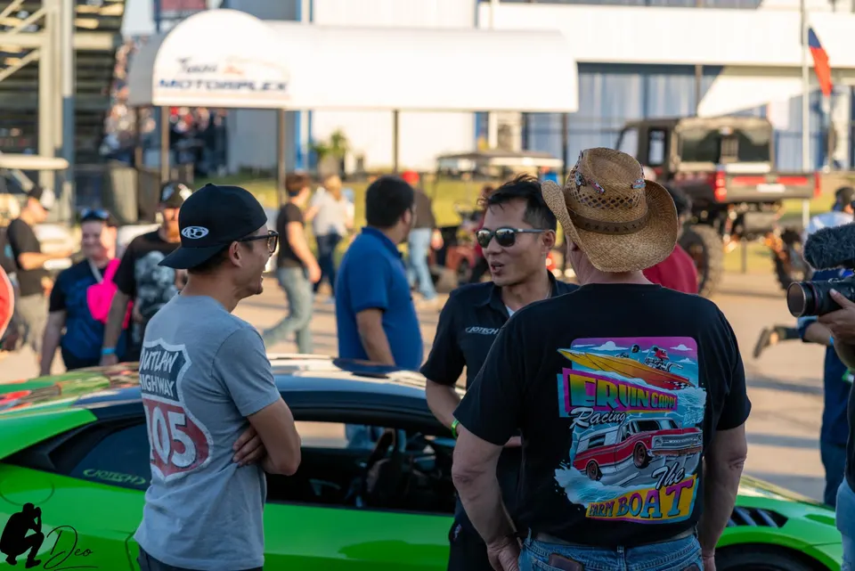 People gathered around a green supercar at an outdoor automotive event at Texas Motorplex, engaging in conversation.