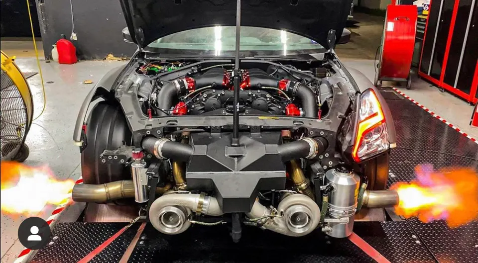 A Nissan GT-R on a dyno with its hood open, showcasing a twin-turbo engine and flames shooting from the exhaust.