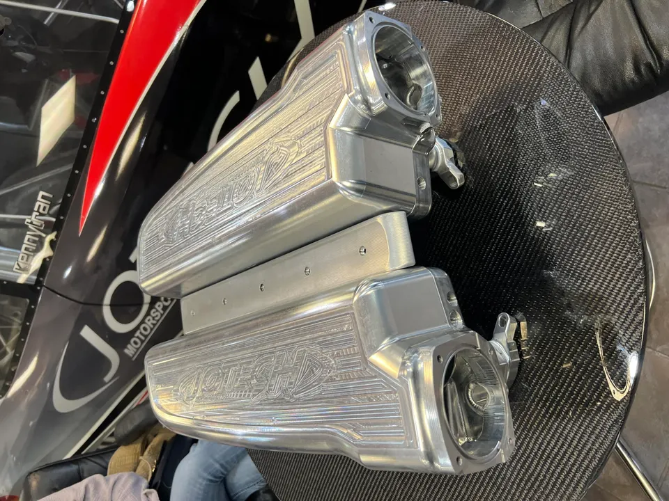 Billet intake manifolds on a carbon fiber table, with a Jotech Motorsports race car in the background.