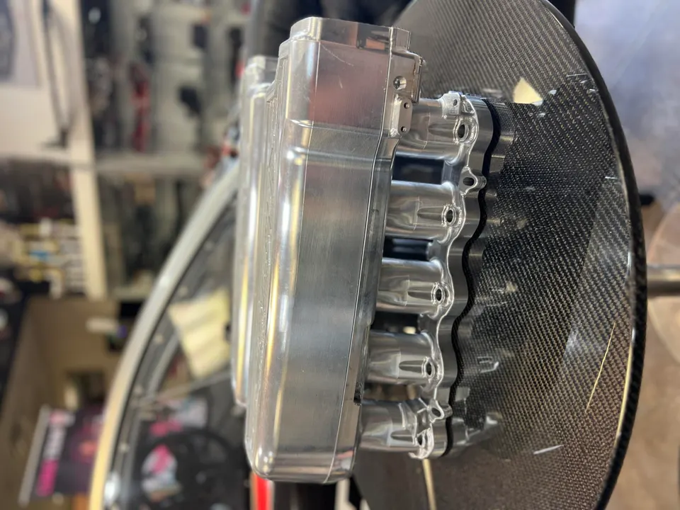A close-up of a billet aluminum intake manifold on a carbon fiber surface in a performance tuning shop.