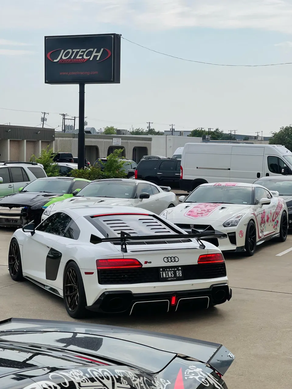 White Audi R8 with an aftermarket wing and a custom-wrapped Nissan GT-R parked outside Jotech Motorsports.