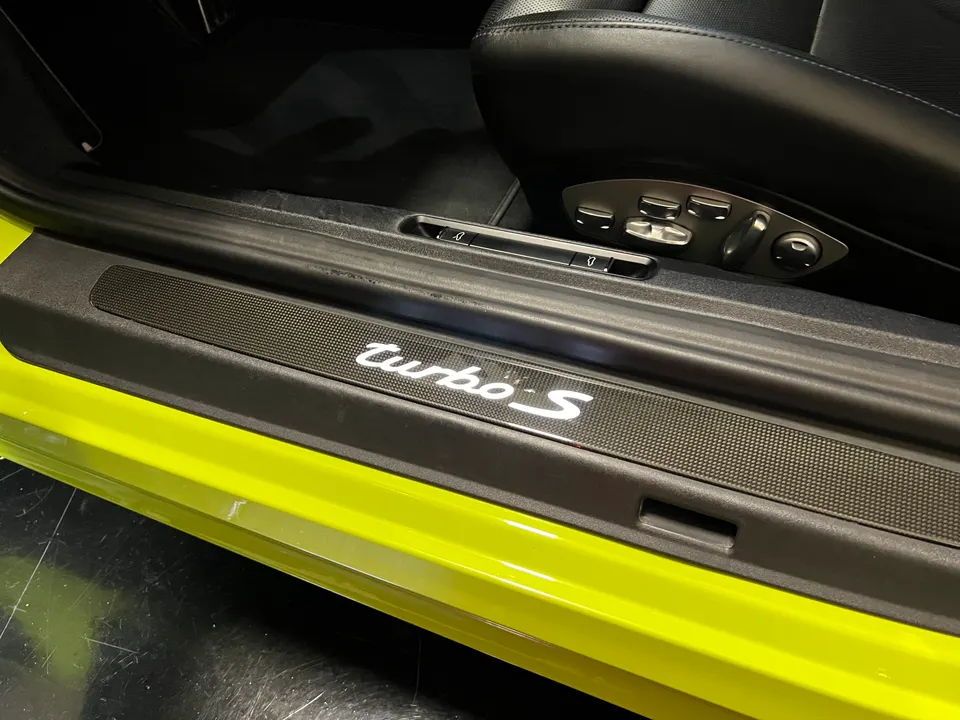 Close-up of a Porsche Turbo S carbon fiber door sill with illuminated lettering and yellow exterior paint.
