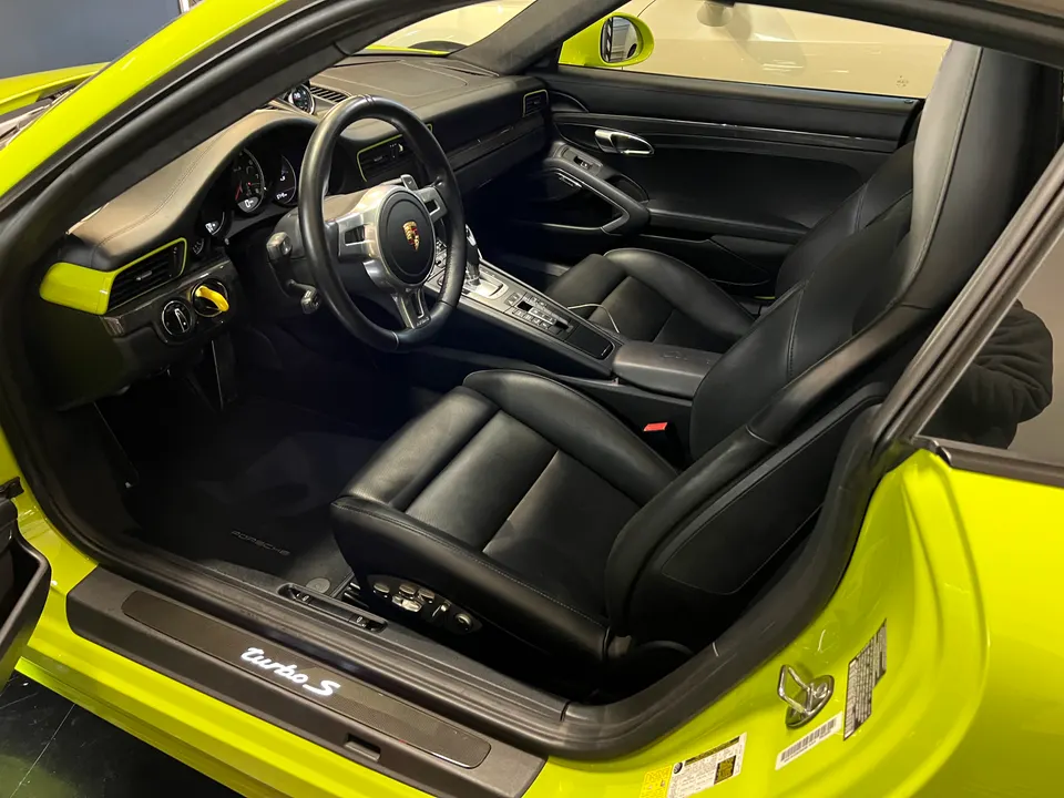 Interior view of a yellow Porsche 911 Turbo S, showcasing black leather seats, steering wheel, and dashboard.