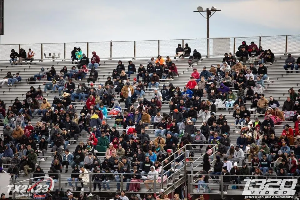 Spectators fill the grandstands at the TX2K23 motorsports event, watching the action on the track.