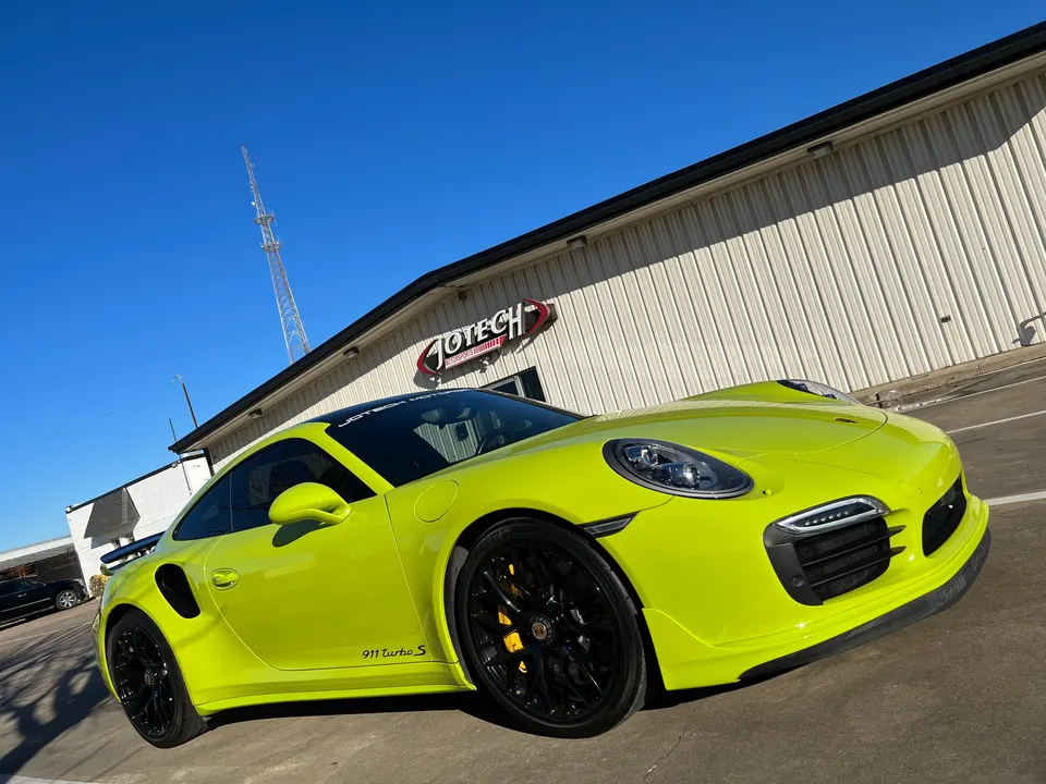 Lime green Porsche 911 Turbo S parked outside Jotech Motorsports building on a sunny day.