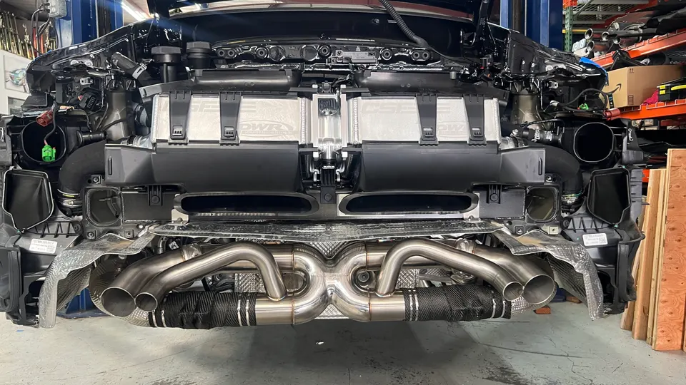 Rear view of a performance car on a lift in a shop, showcasing an aftermarket exhaust system and intercoolers during installation.