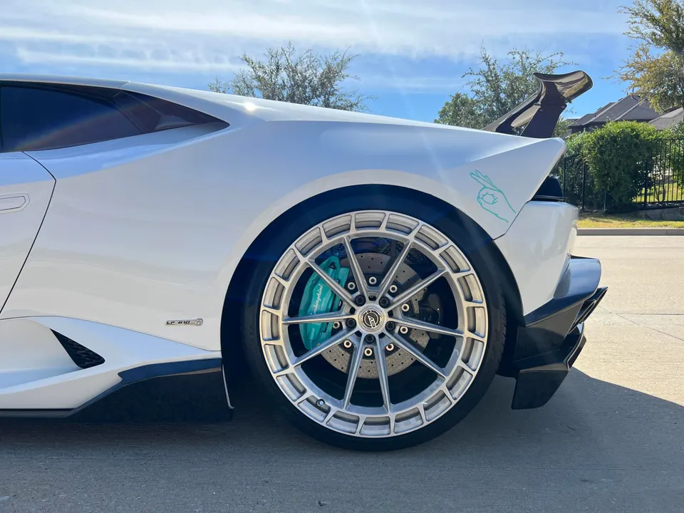 Side view of a white Lamborghini Huracan with custom silver wheels, teal brake calipers, and a carbon fiber rear wing.