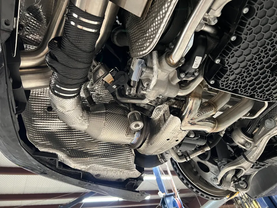 Undercarriage view of a performance car showing a Fabspeed exhaust system with heat-wrapped downpipes during installation.