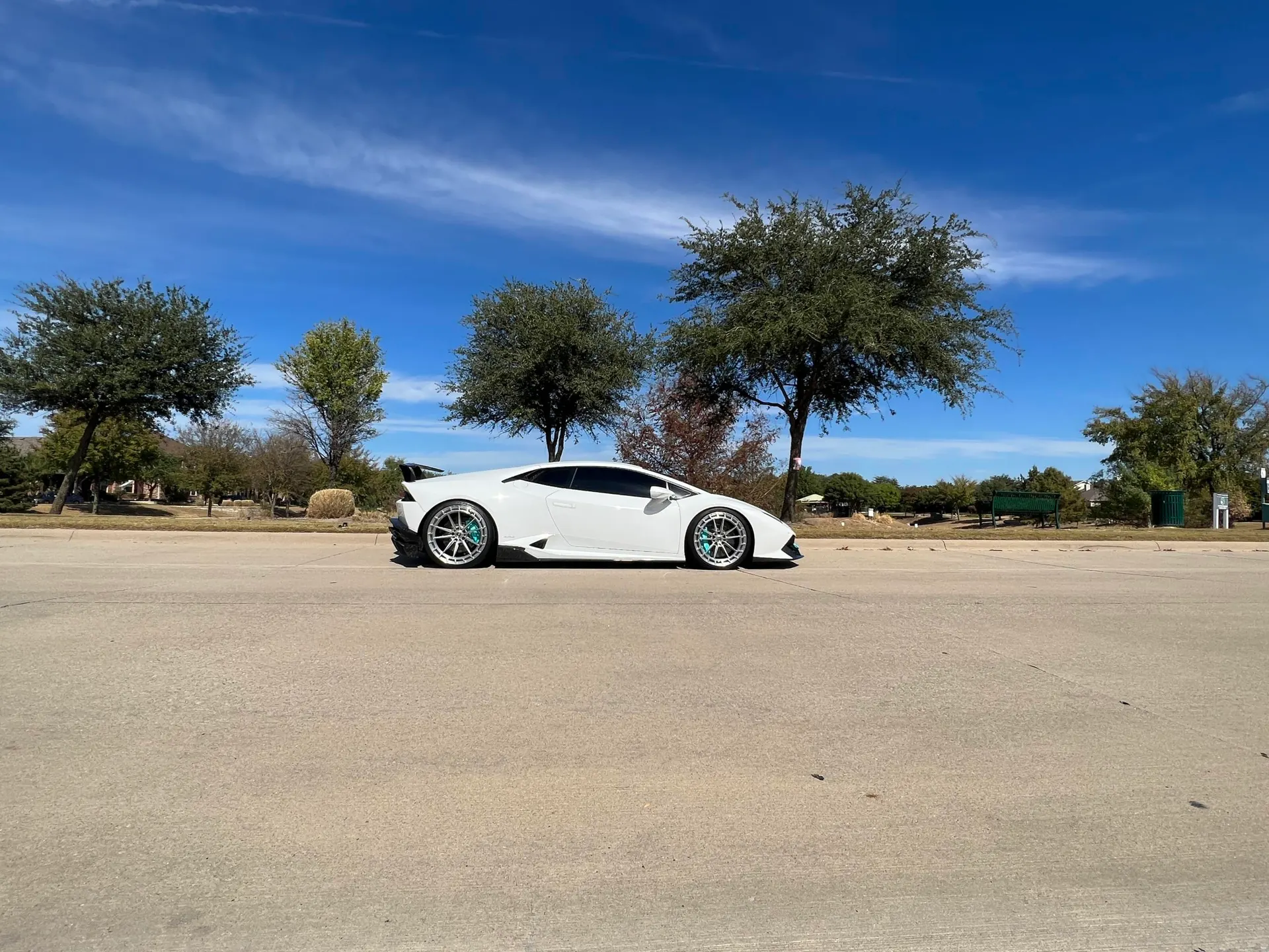 White Lamborghini Huracan with custom wheels and a rear wing parked on a sunny day.