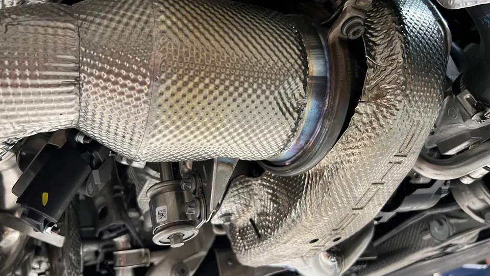 Close-up of a heat-shielded turbocharger or downpipe in a performance car's engine bay.