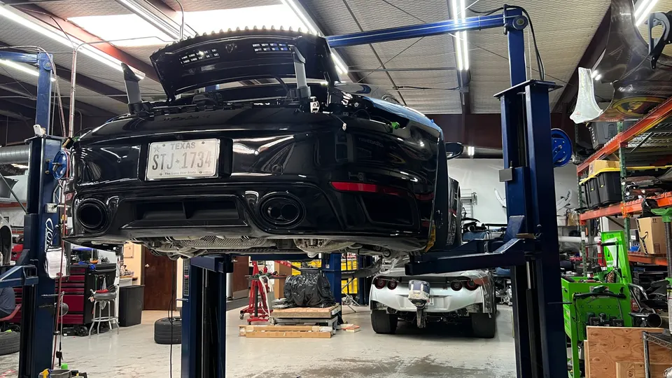 Black Porsche 911 on a lift in a performance tuning shop, showcasing its rear and exhaust system.