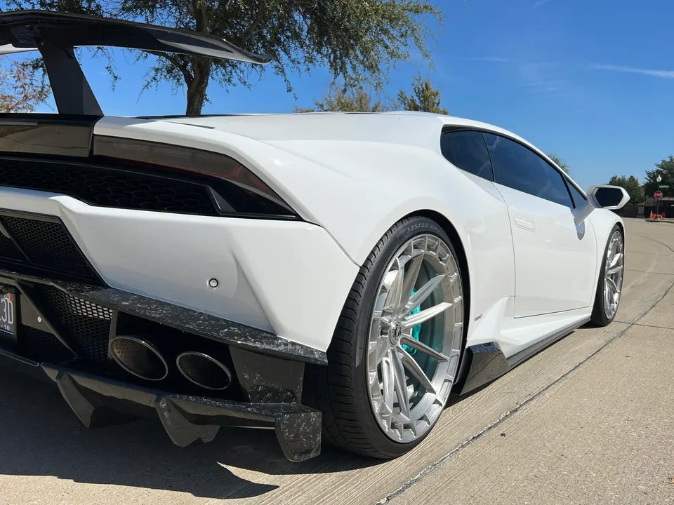 A white Lamborghini Huracan with a large carbon fiber wing, custom wheels, and a rear diffuser parked outdoors.