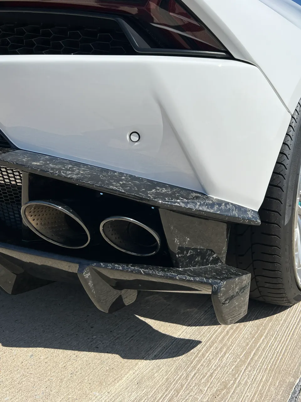 Close-up of a white Lamborghini's rear bumper featuring a carbon fiber diffuser and dual exhaust tips.