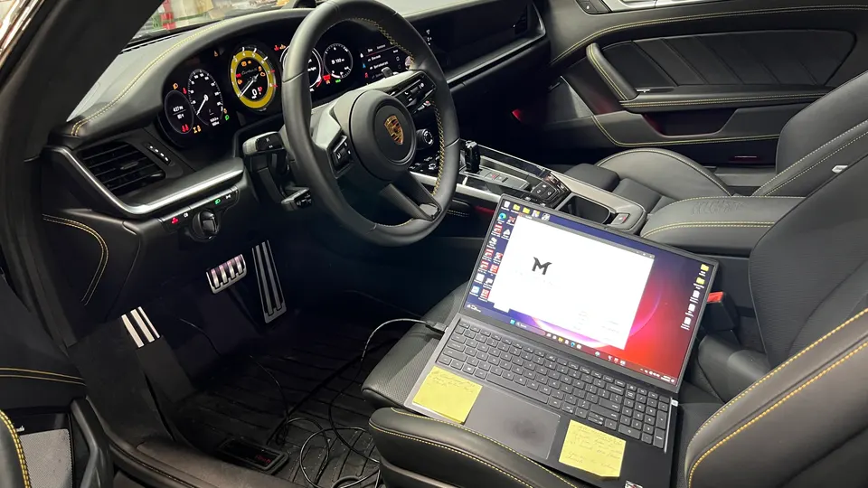 Interior view of a Porsche with a laptop connected for performance tuning, showing the dashboard and steering wheel.