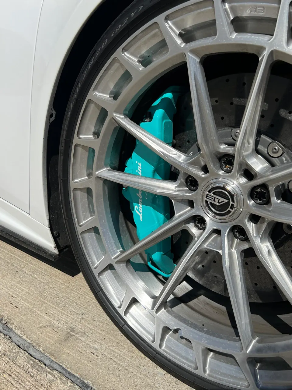 A close-up of a Lamborghini wheel with a silver multi-spoke design and a vibrant turquoise brake caliper.