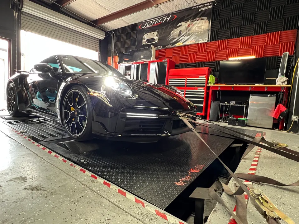 Black Porsche 911 strapped to a dynamometer in a performance tuning shop, ready for a dyno run.