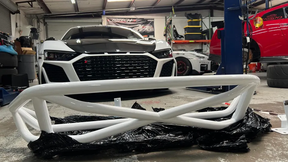 White roll bar in the foreground with a white Audi R8 and other performance cars in a Jotech Motorsports shop.