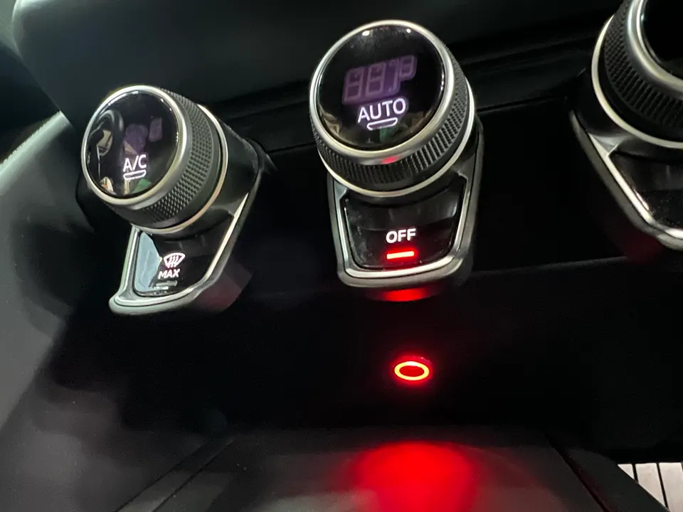 Close-up of a car's interior showing climate control knobs, digital display, and red accent lighting.