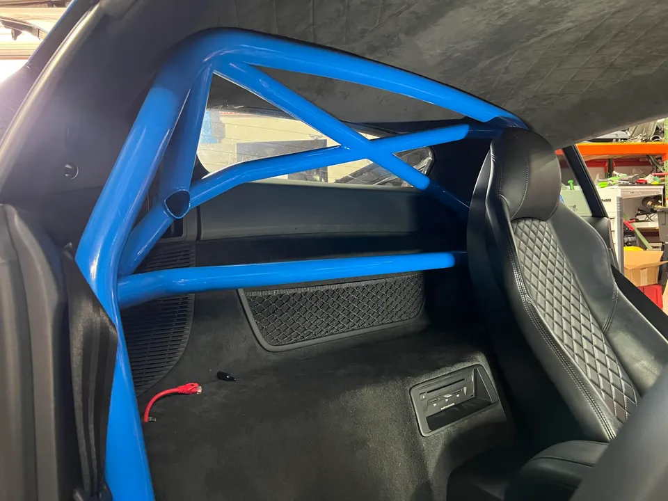 Blue roll cage installed in the rear interior of a performance car, featuring a quilted sports seat.