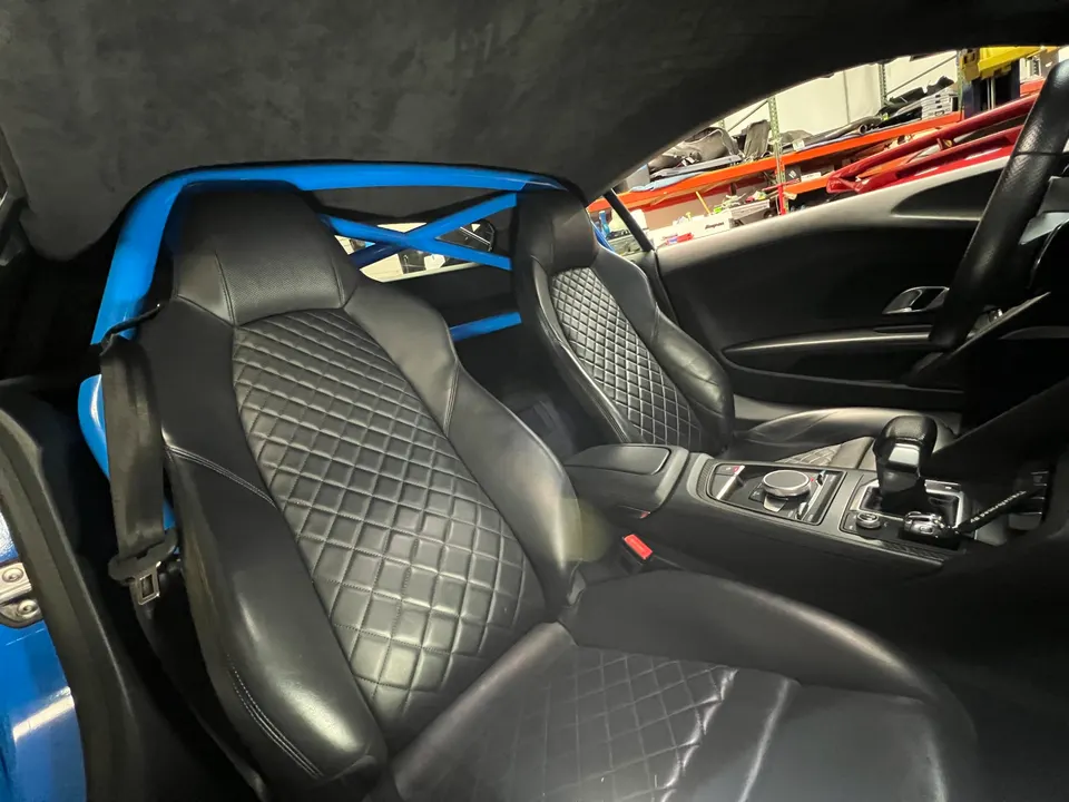 Interior view of an Audi R8 with black quilted leather seats and a bright blue roll bar.