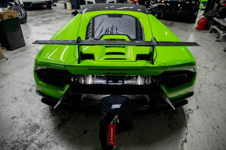 Bright green Lamborghini Huracan in a shop, rear view showing twin turbochargers and a large aftermarket rear wing.