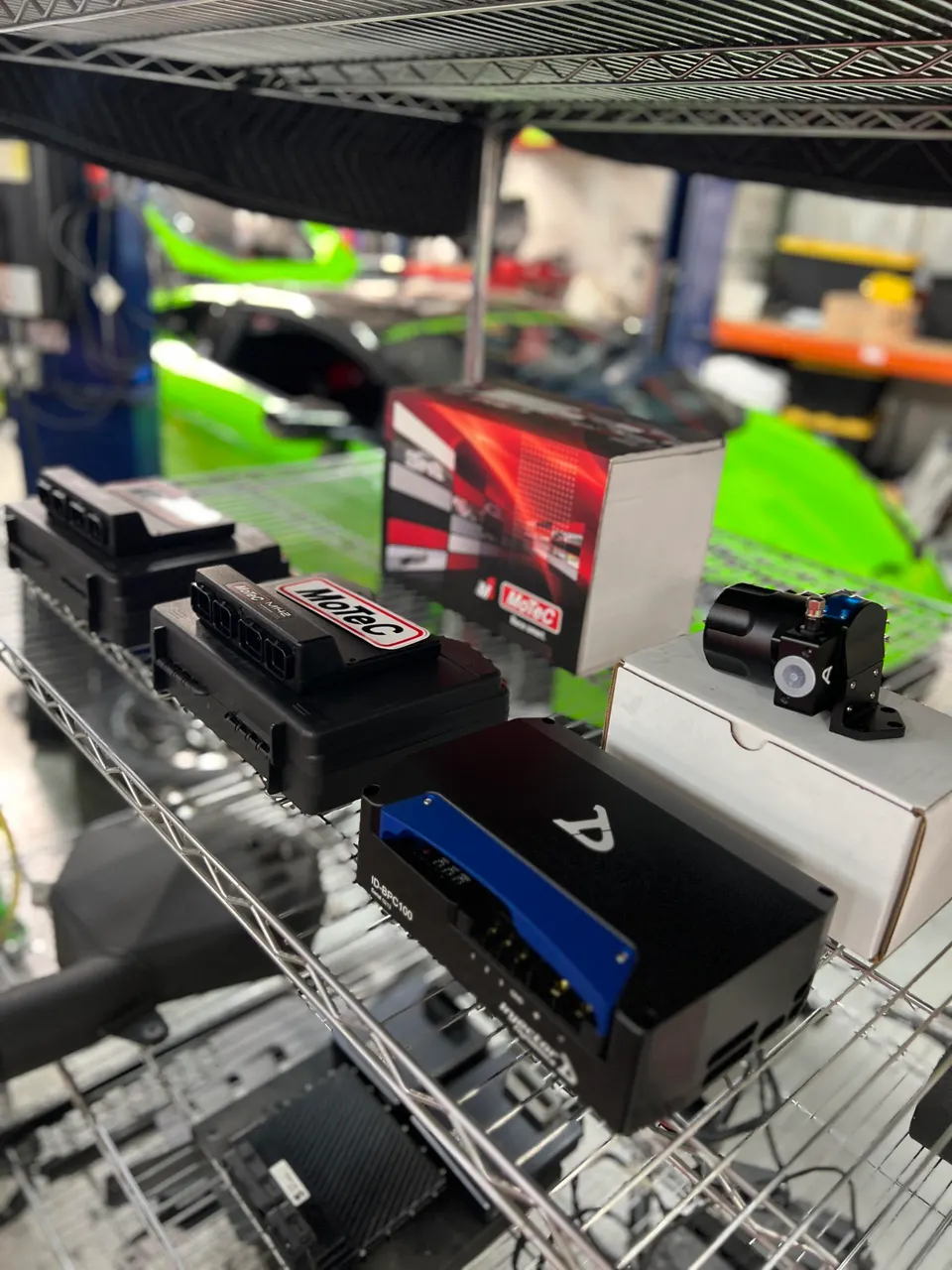 MoTeC ECUs and Injector Dynamics fuel pump controller on a shelf in a performance tuning shop with a green supercar.