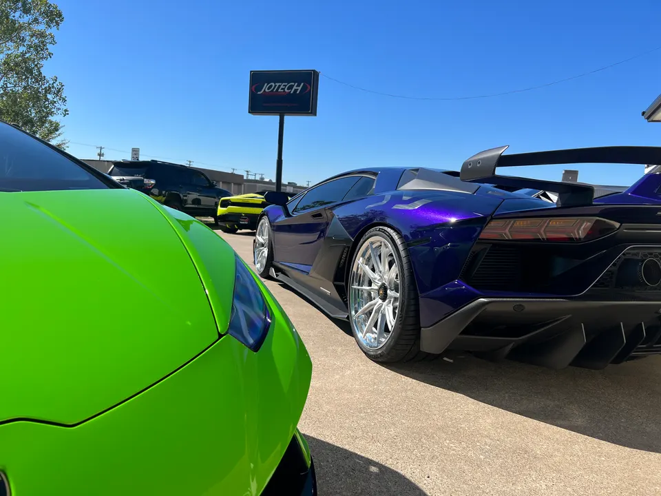 Purple Lamborghini Aventador and green Lamborghini Huracan parked outside Jotech Motorsports performance shop.