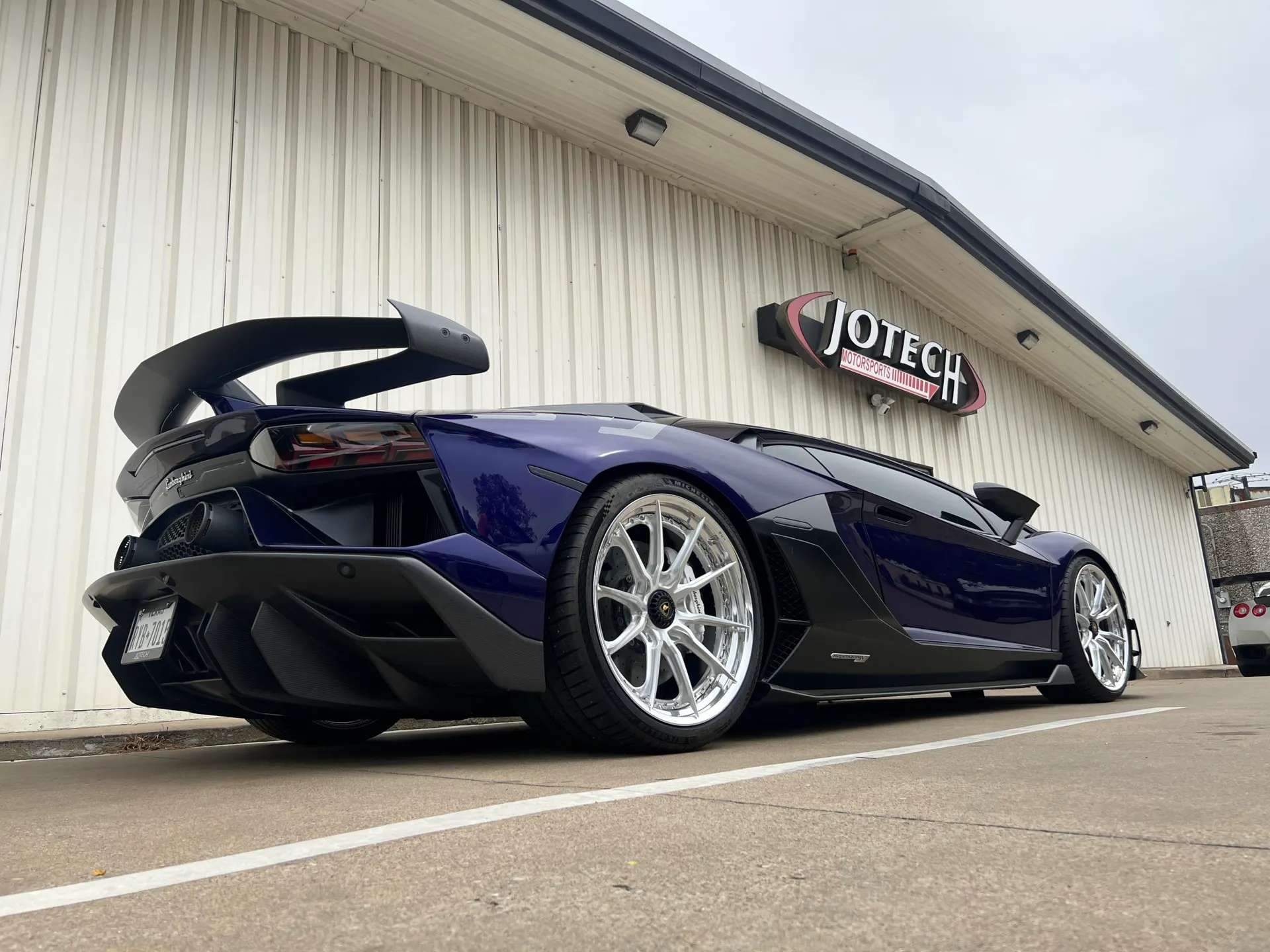 Purple Lamborghini Aventador with aftermarket wing and custom wheels parked outside Jotech Motorsports shop.