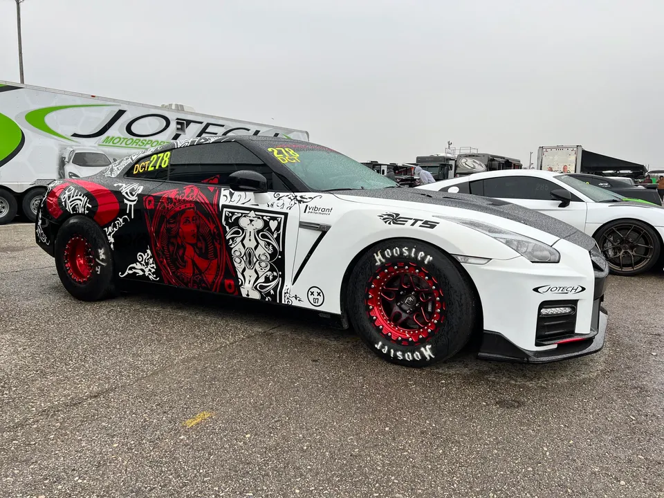A highly modified white and black Nissan GT-R drag car with red custom wheels and Hoosier tires at a track event.