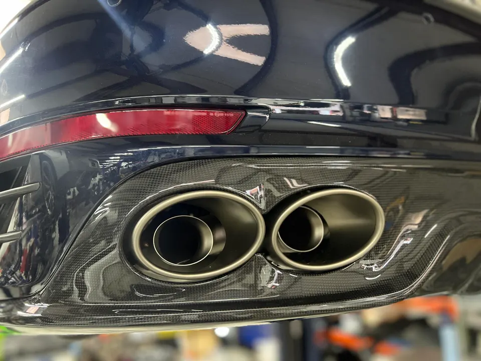 Close-up of a car's rear bumper featuring dual exhaust tips and a glossy carbon fiber diffuser.