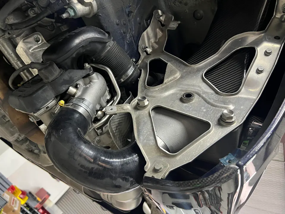 Undercarriage view of a performance car showing turbo system, boost piping, and carbon fiber components.