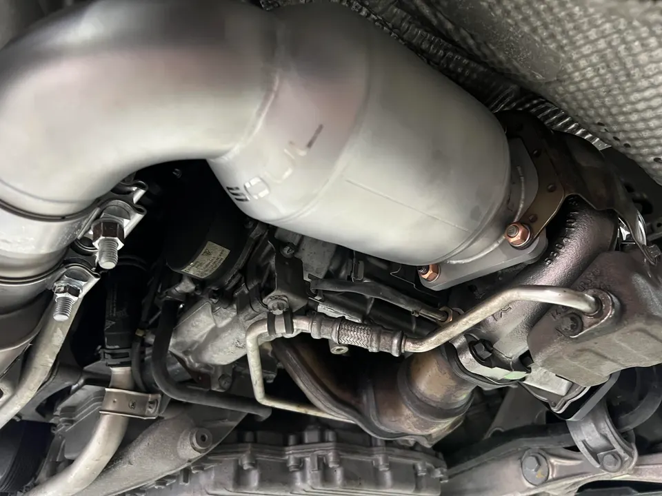 Close-up view of an aftermarket exhaust system, including downpipes and catalytic converters, installed on the underside of a performance car.