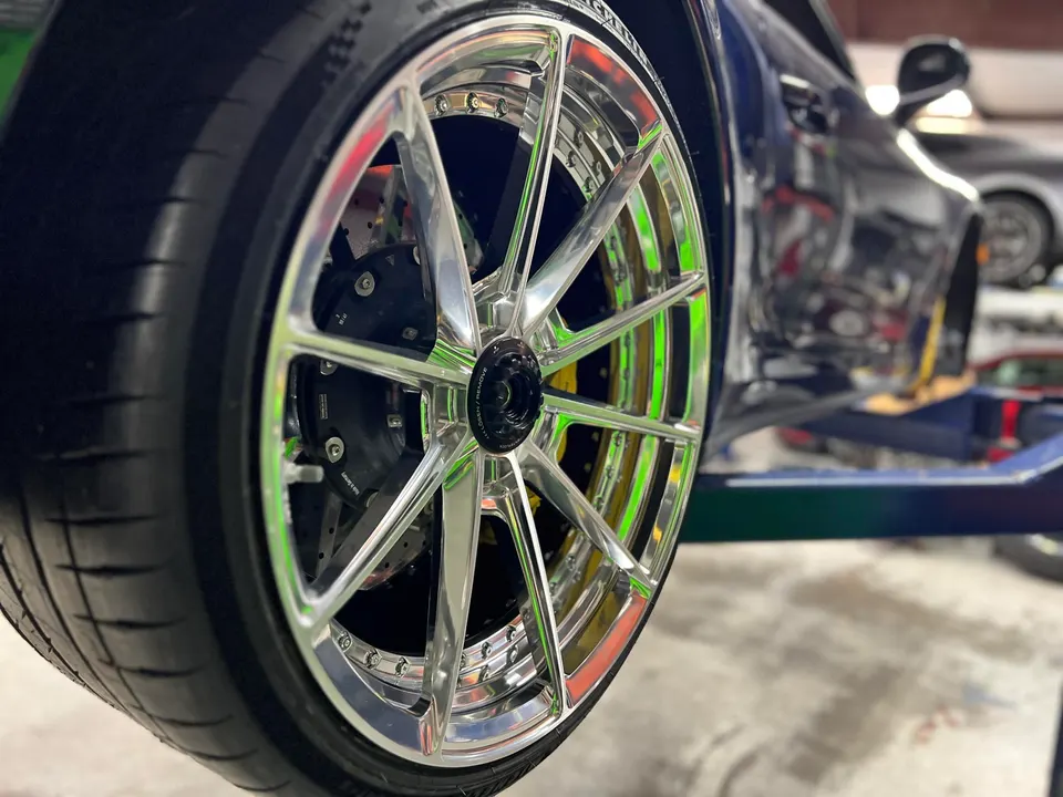 Close-up of a custom chrome wheel, performance tire, and large brake caliper on a car lifted in a shop.