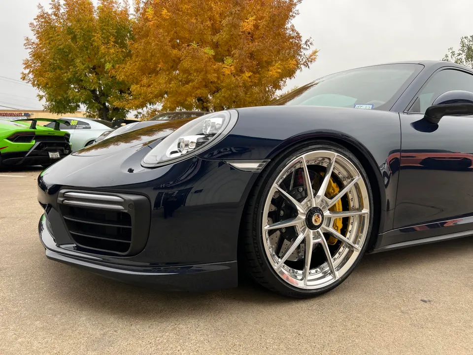 Dark blue Porsche 911 with custom polished multi-spoke wheels and yellow brake calipers, parked outdoors.