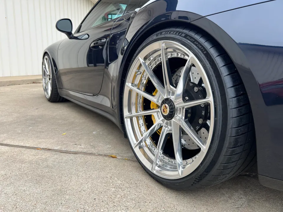 Close-up of a black Porsche 911 with custom chrome wheels, Michelin tires, and yellow brake calipers.