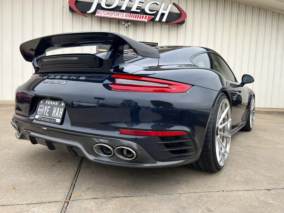 Dark blue Porsche 911 Turbo S with a large rear wing, custom wheels, and aftermarket exhaust parked outside Jotech Motorsports.