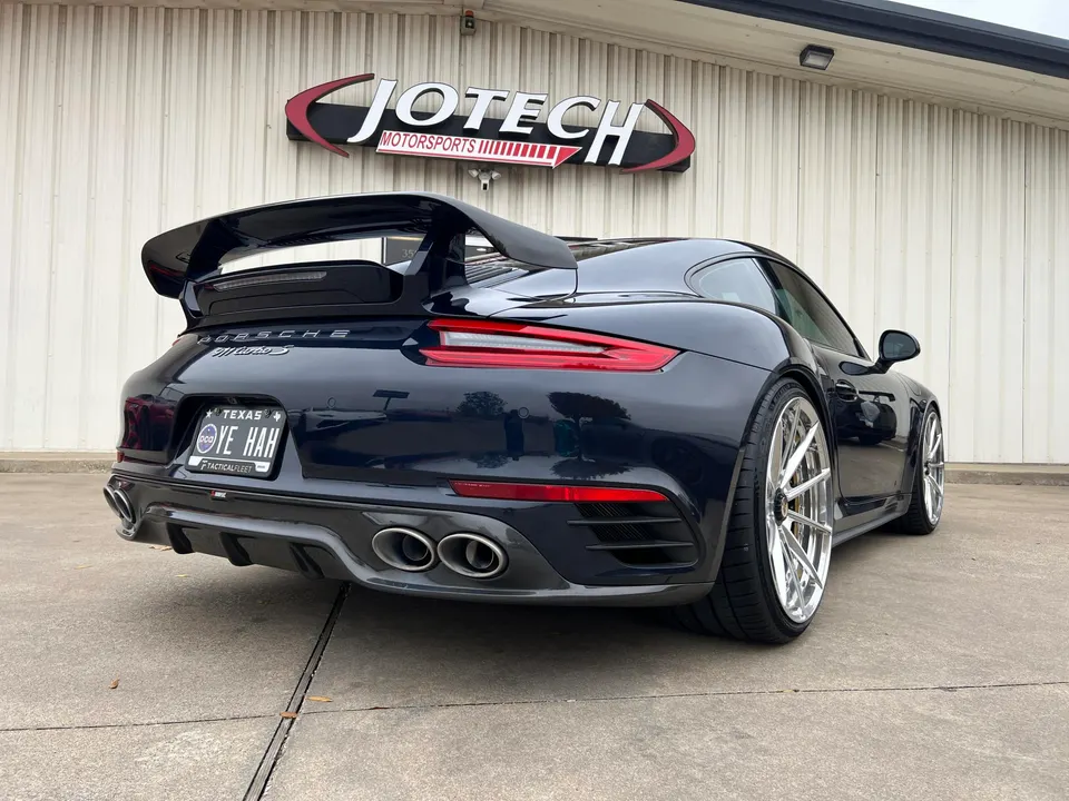 Dark blue Porsche 911 Turbo S with custom chrome wheels and a large rear wing parked outside Jotech Motorsports.
