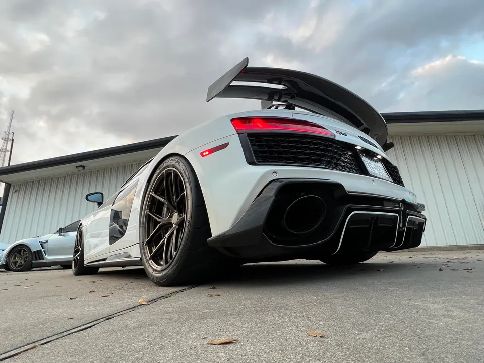 White Audi R8 with a large carbon fiber rear wing, aggressive diffuser, and custom wheels parked outdoors.