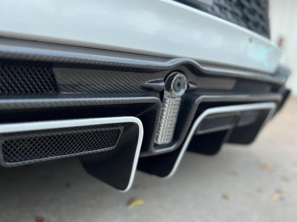 A close-up of a car's carbon fiber rear diffuser and bumper.