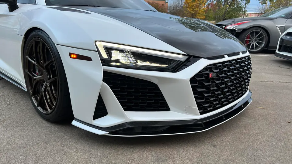 A white Audi R8 with a black carbon fiber hood, custom wheels, and an aggressive front splitter parked outdoors.