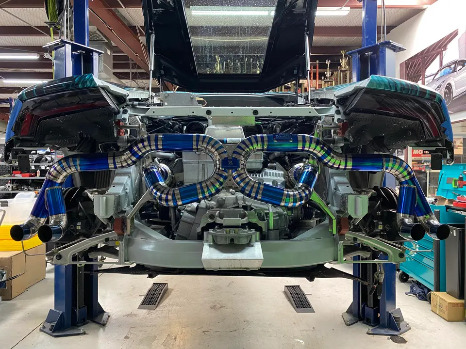 Rear view of a McLaren on a lift in a shop, showcasing a custom titanium exhaust system installation.