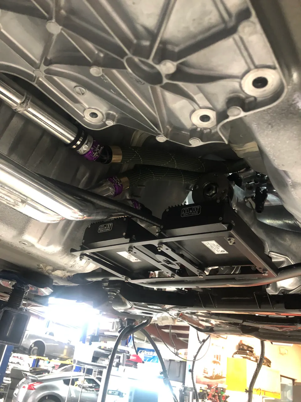 Underside view of a performance car on a lift, showcasing aftermarket ignition modules and drivetrain components.