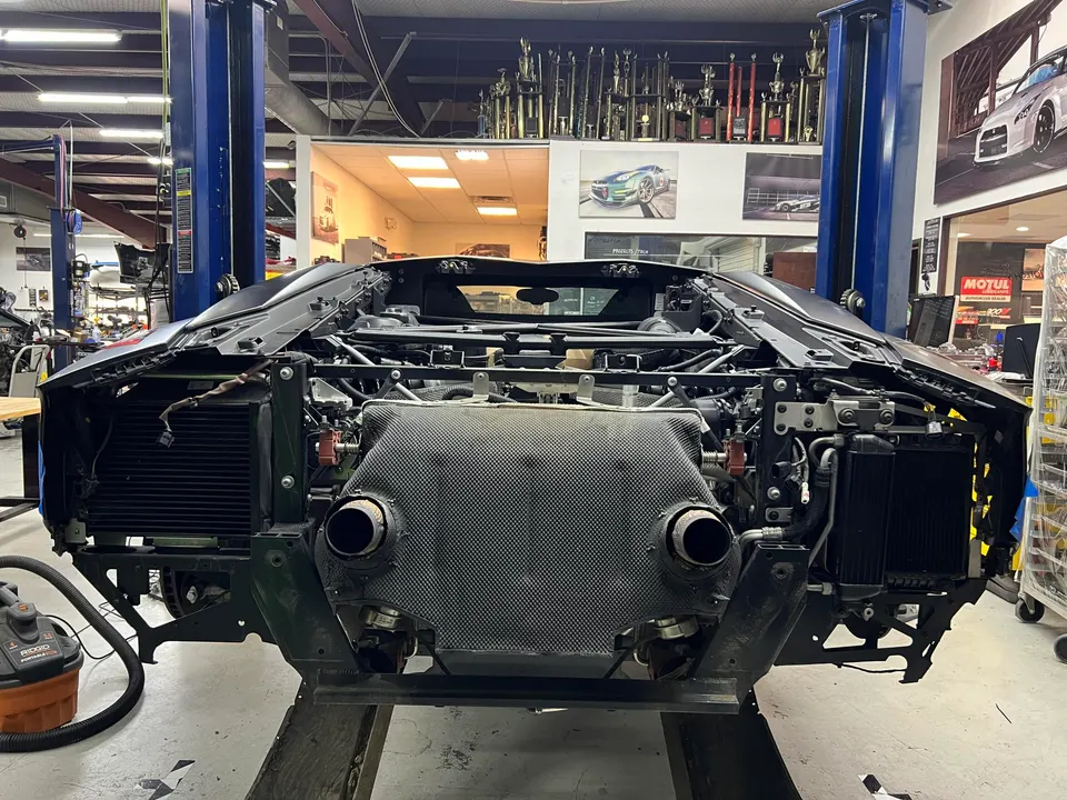 Rear view of a Lamborghini Aventador undergoing disassembly in a performance tuning shop, showing the exhaust system and carbon fiber components.