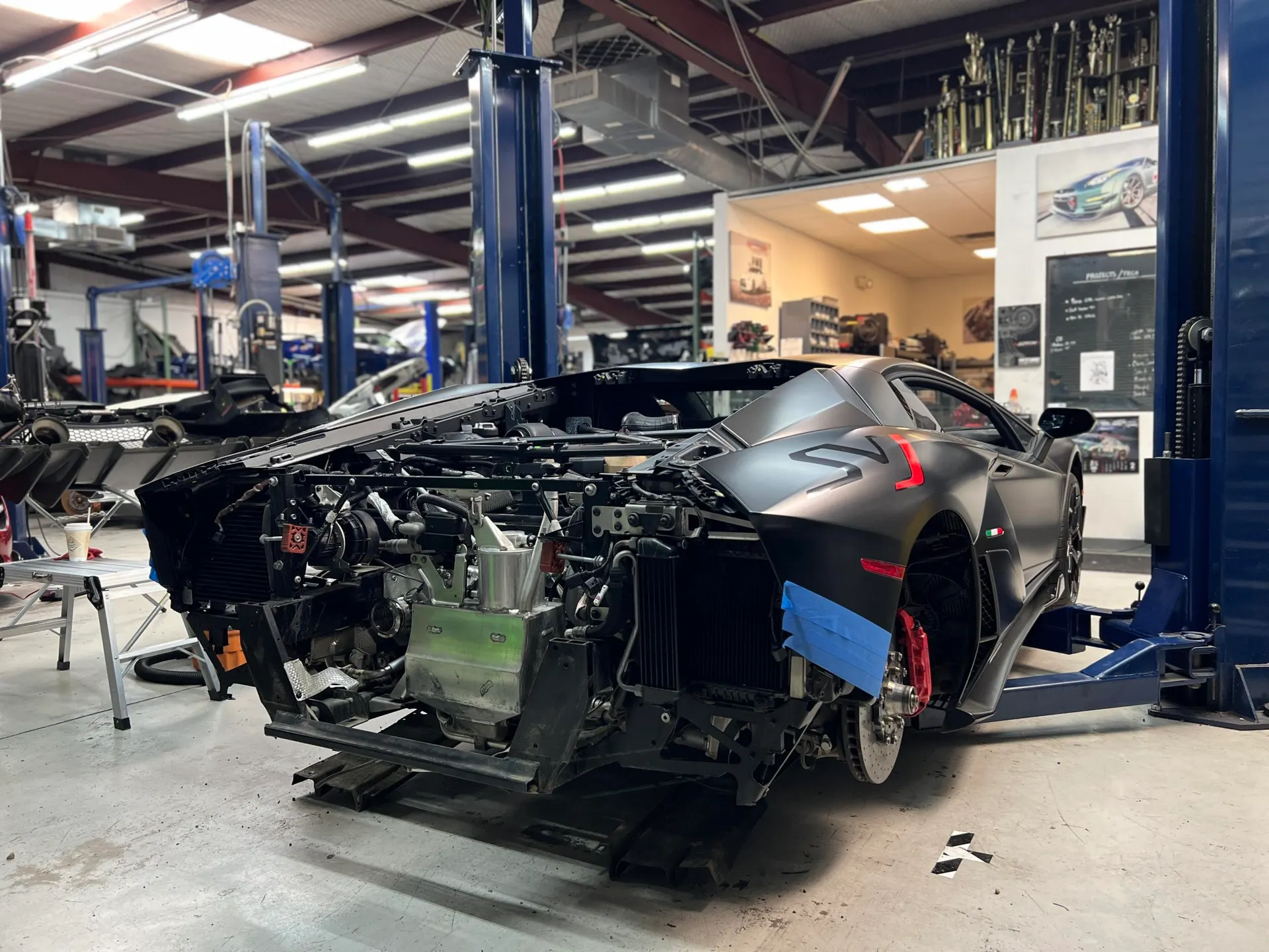 Matte black Lamborghini Aventador undergoing extensive work on a car lift in a performance tuning shop.